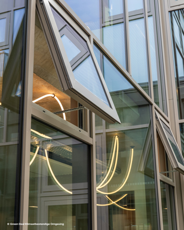 Moderne bygningsfacade med kantede glasvinduer, hvoraf nogle er åbne, reflekterer neonlys og fremviser moderne arkitektonisk design.